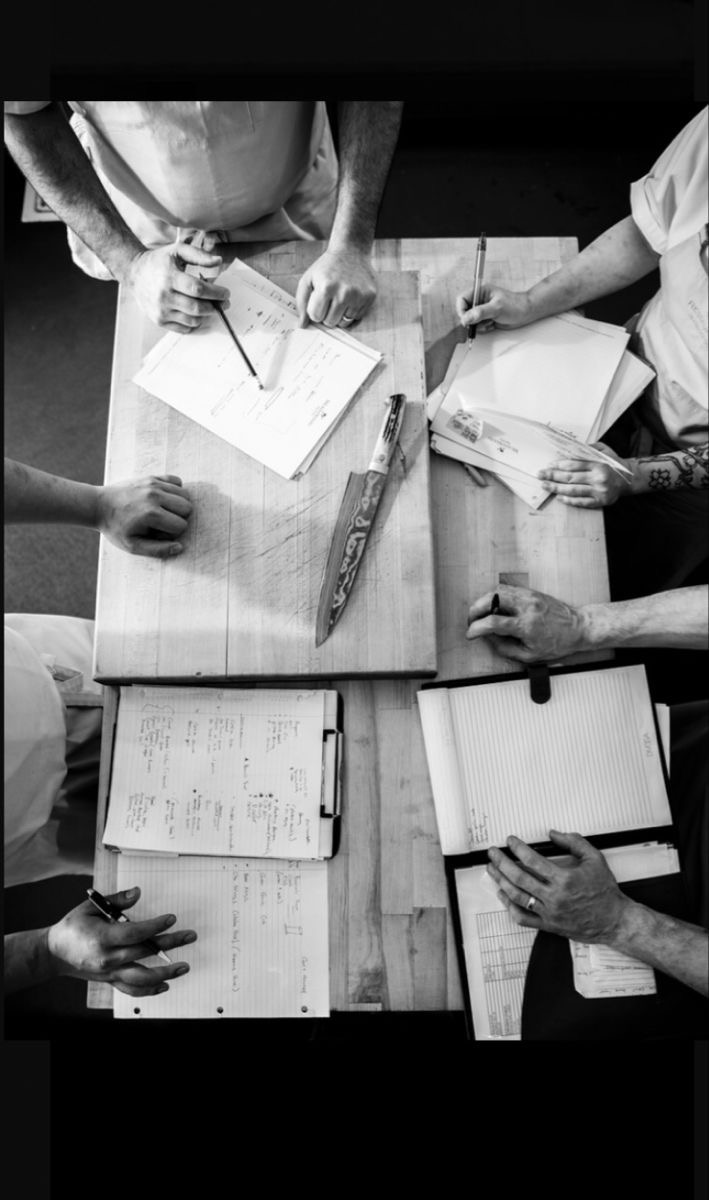 Black-and-white photograph of chefs planning together around a kitchen table